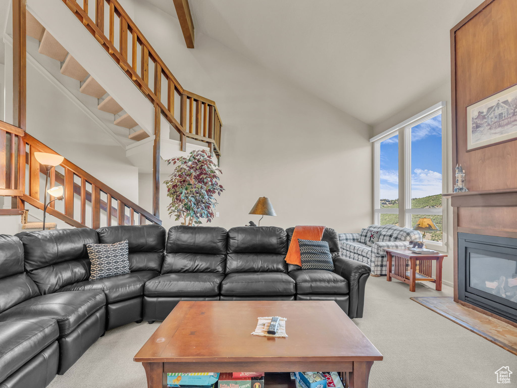 Carpeted living area with high vaulted ceiling, a glass covered fireplace, and stairway