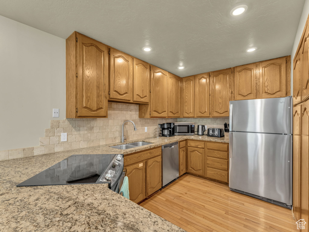 Kitchen with stainless steel appliances, light wood-style floors, tasteful backsplash, recessed lighting, and brown cabinetry