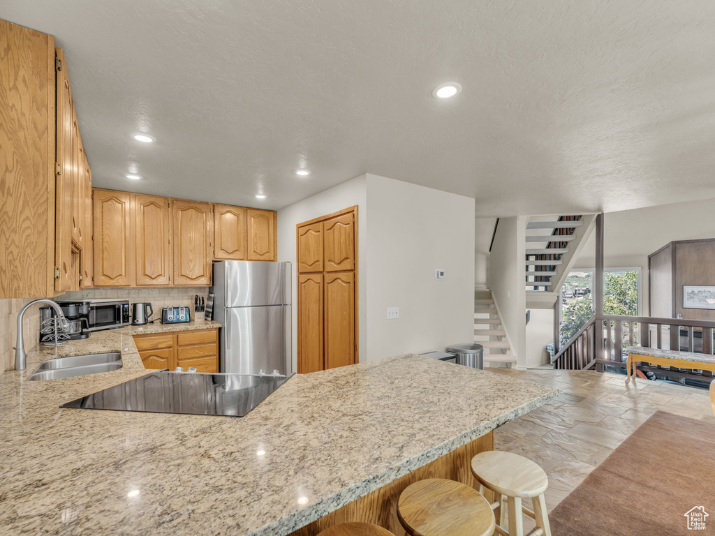 Kitchen with stainless steel appliances, a peninsula, a breakfast bar area, light stone counters, and stone tile flooring