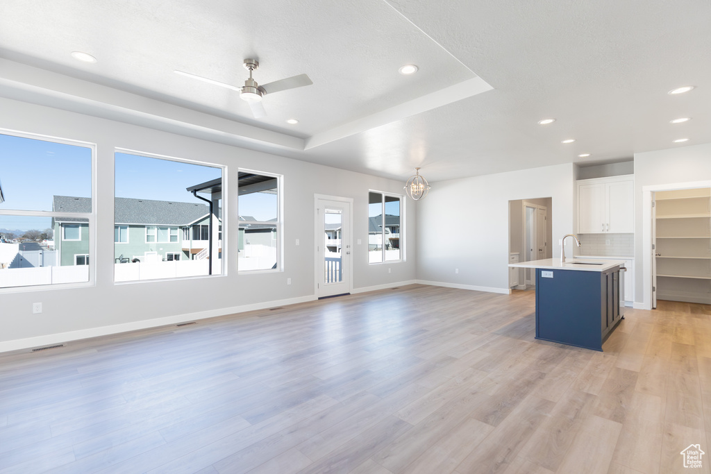 Unfurnished living room with ceiling fan, recessed lighting, light wood-style floors, and a tray ceiling