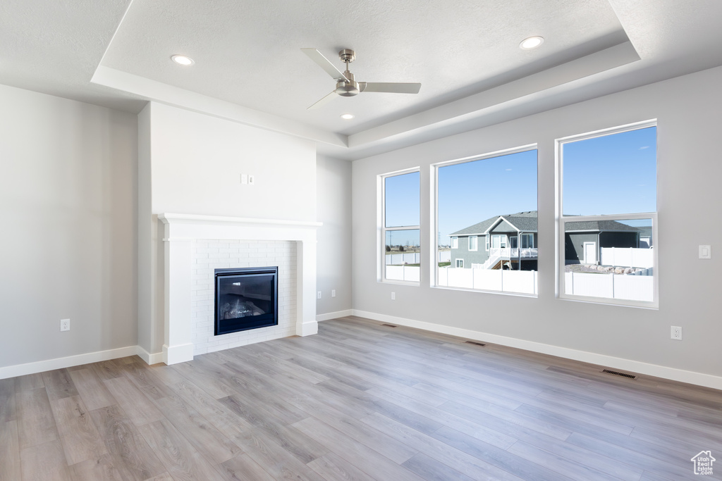 Unfurnished living room with a tray ceiling, a ceiling fan, wood finished floors, a fireplace, and recessed lighting