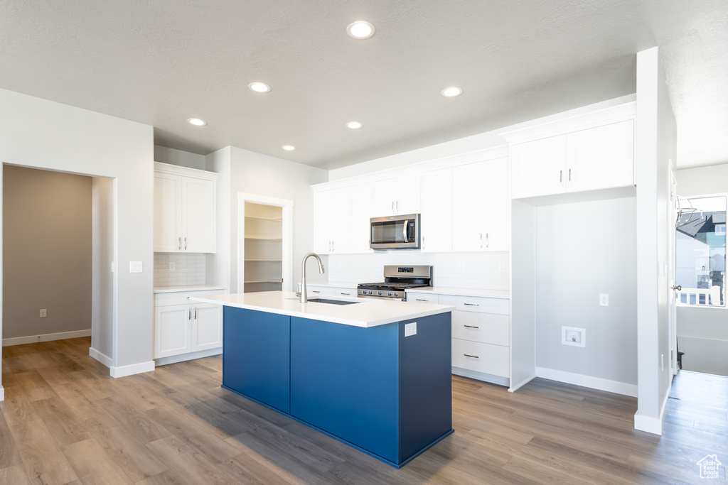 Kitchen featuring appliances with stainless steel finishes, backsplash, a kitchen island with sink, white cabinets, and recessed lighting