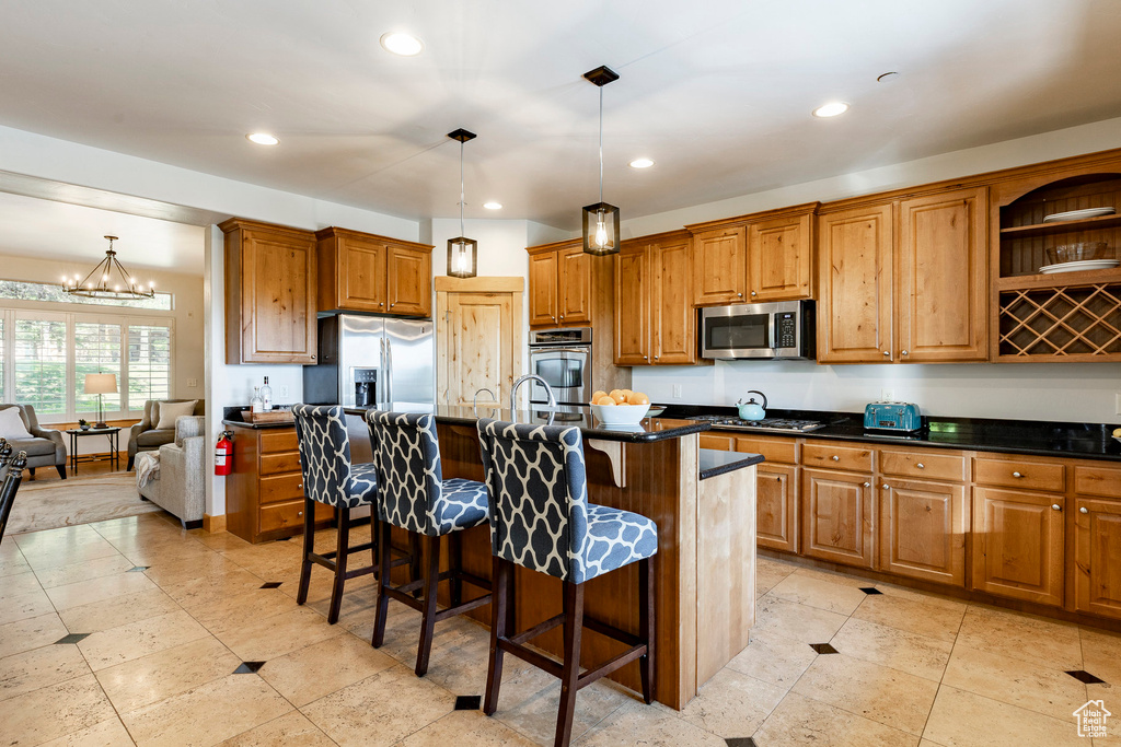 Kitchen with stainless steel appliances, dark countertops, brown cabinetry, a kitchen breakfast bar, and recessed lighting