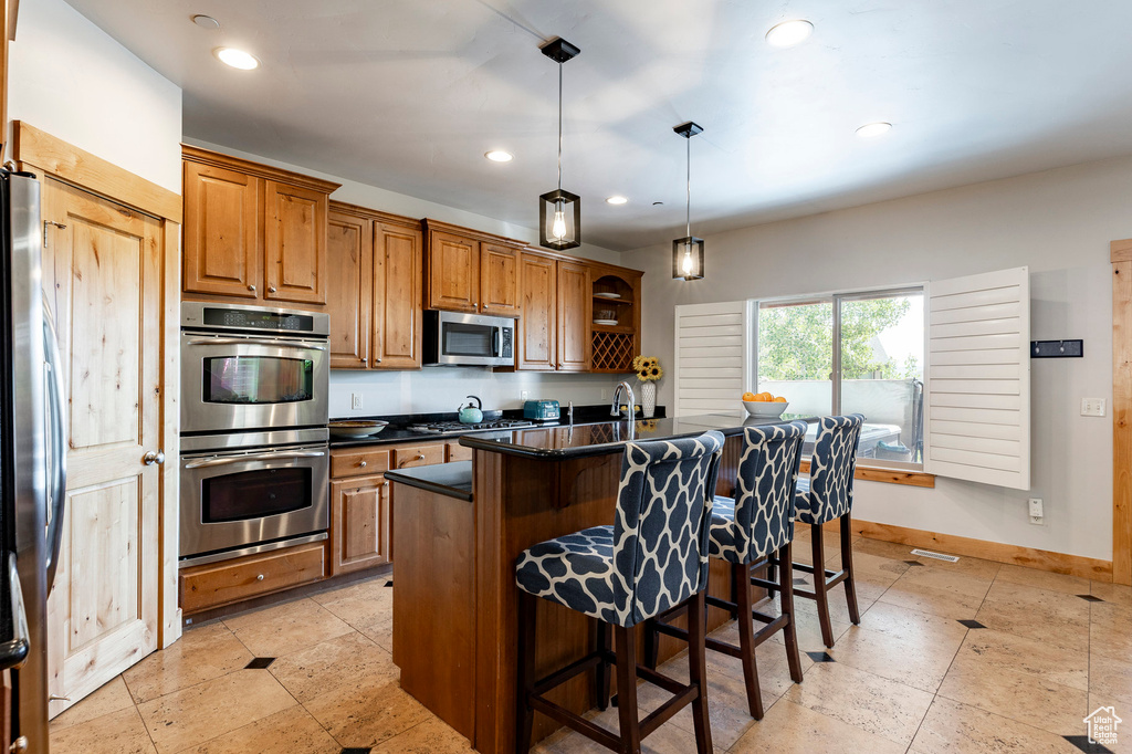 Kitchen with appliances with stainless steel finishes, dark countertops, brown cabinets, a breakfast bar, and pendant lighting