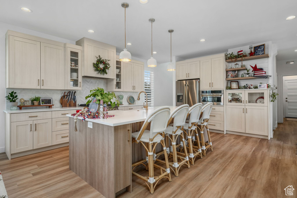 Kitchen with appliances with stainless steel finishes, light countertops, tasteful backsplash, open shelves, and an island with sink