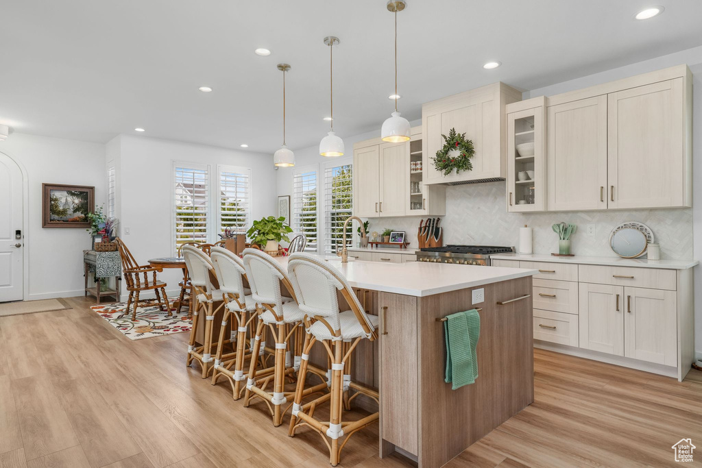 Kitchen with recessed lighting, a center island with sink, light wood-type flooring, a breakfast bar, and light countertops