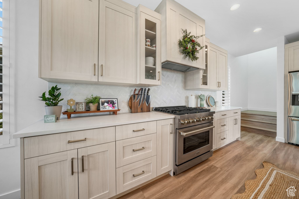 Kitchen with stainless steel appliances, light countertops, tasteful backsplash, glass insert cabinets, and recessed lighting