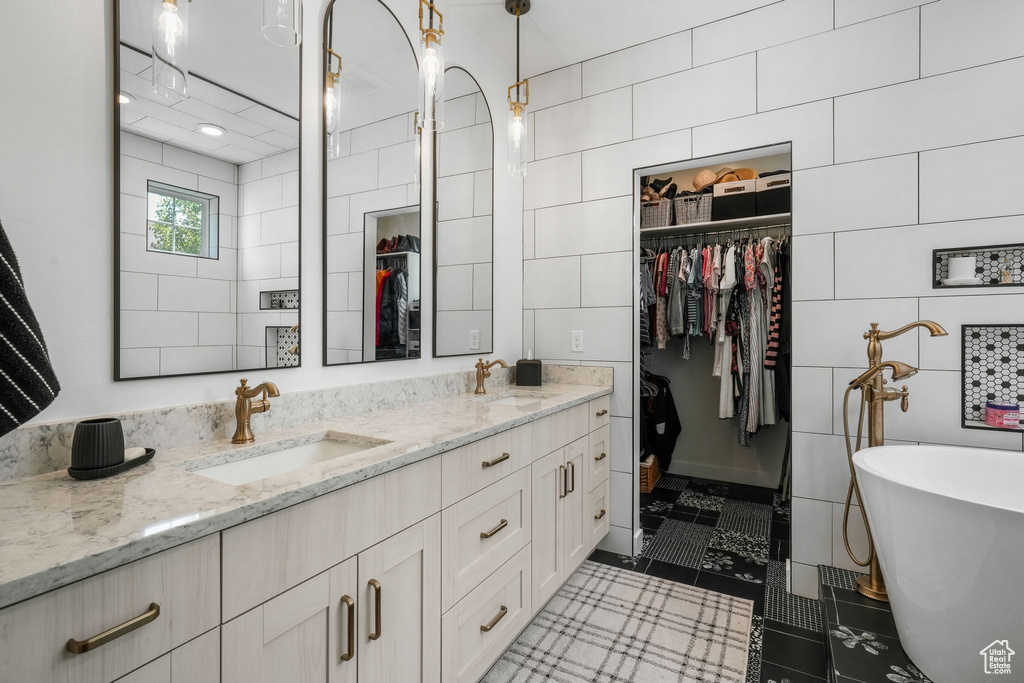 Bathroom featuring a spacious closet, a soaking tub, double vanity, tile walls, and tile patterned flooring