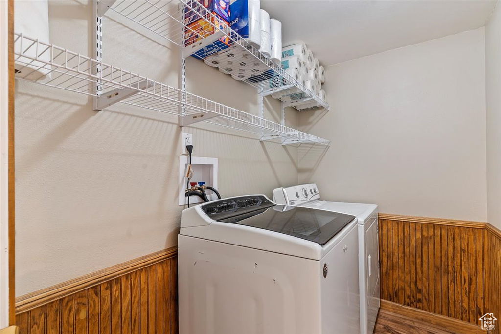 Laundry area with washer and clothes dryer, a wainscoted wall, wooden walls, and wood finished floors