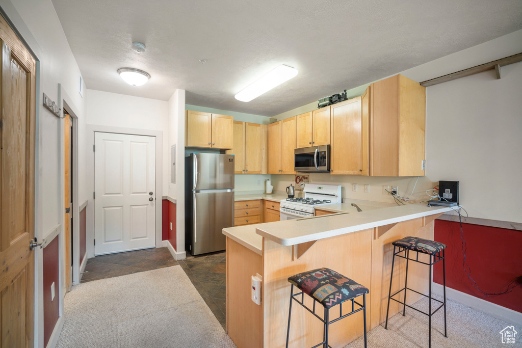 Kitchen featuring appliances with stainless steel finishes, light brown cabinetry, a peninsula, a kitchen breakfast bar, and light countertops