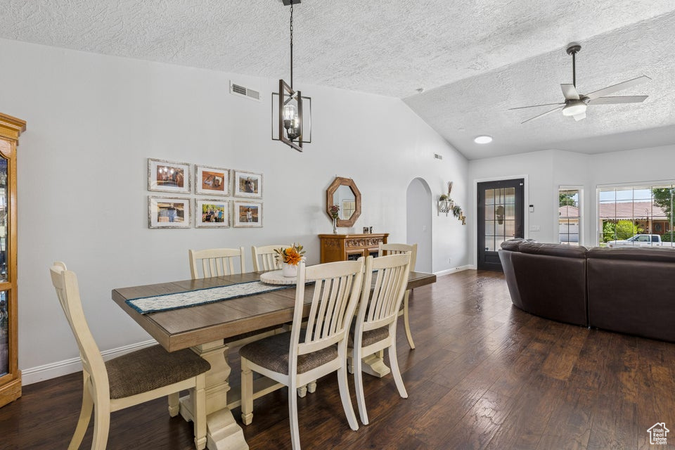 Dining room with a textured ceiling, vaulted ceiling, arched walkways, a ceiling fan, and dark wood-type flooring