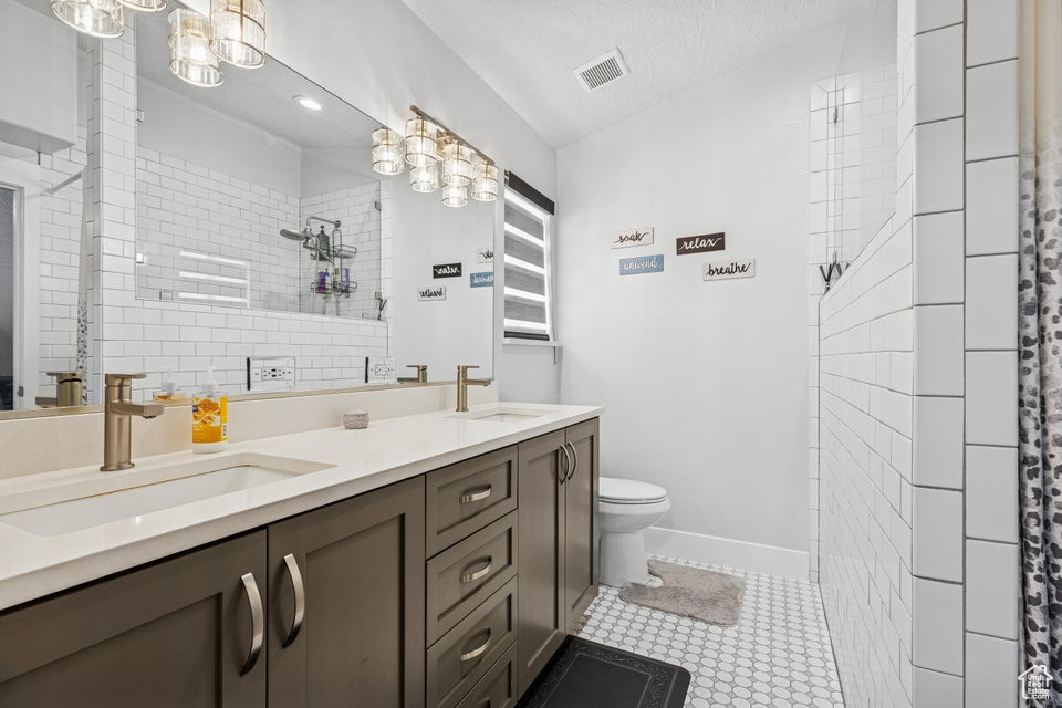 Bathroom featuring double vanity, a tile shower, tile patterned floors, and a textured ceiling