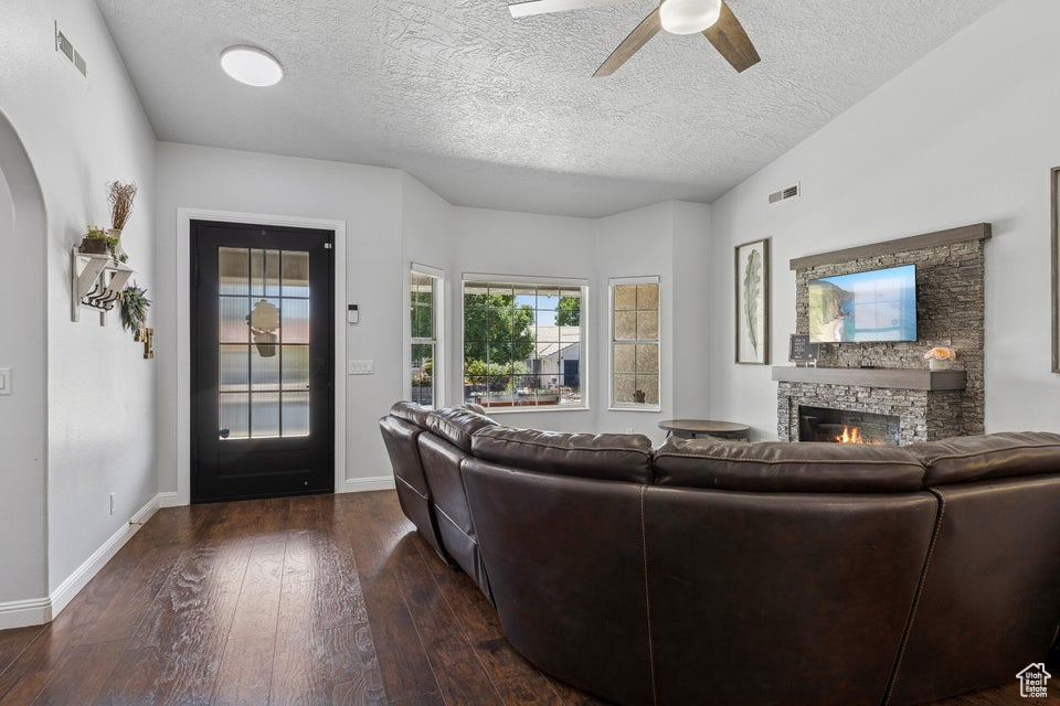 Living area with a fireplace, ceiling fan, dark wood-style floors, arched walkways, and a textured ceiling