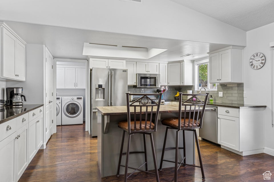 Kitchen featuring appliances with stainless steel finishes, independent washer and dryer, dark wood finished floors, and backsplash