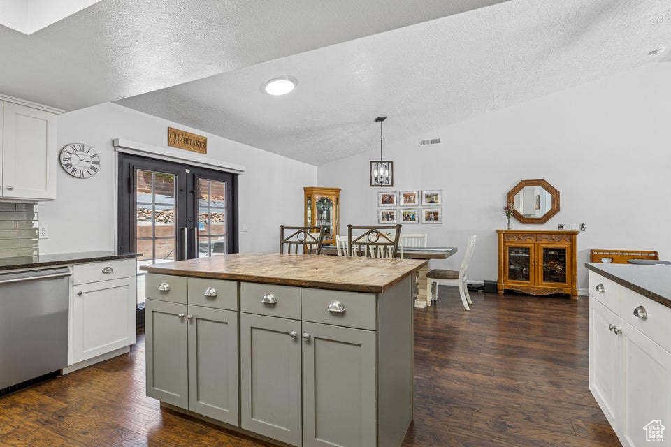 Kitchen featuring stainless steel dishwasher, butcher block counters, vaulted ceiling, a textured ceiling, and dark wood-style floors