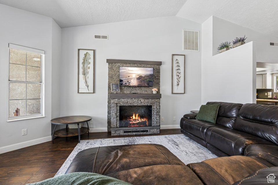 Living room with vaulted ceiling, wood finished floors, and a fireplace
