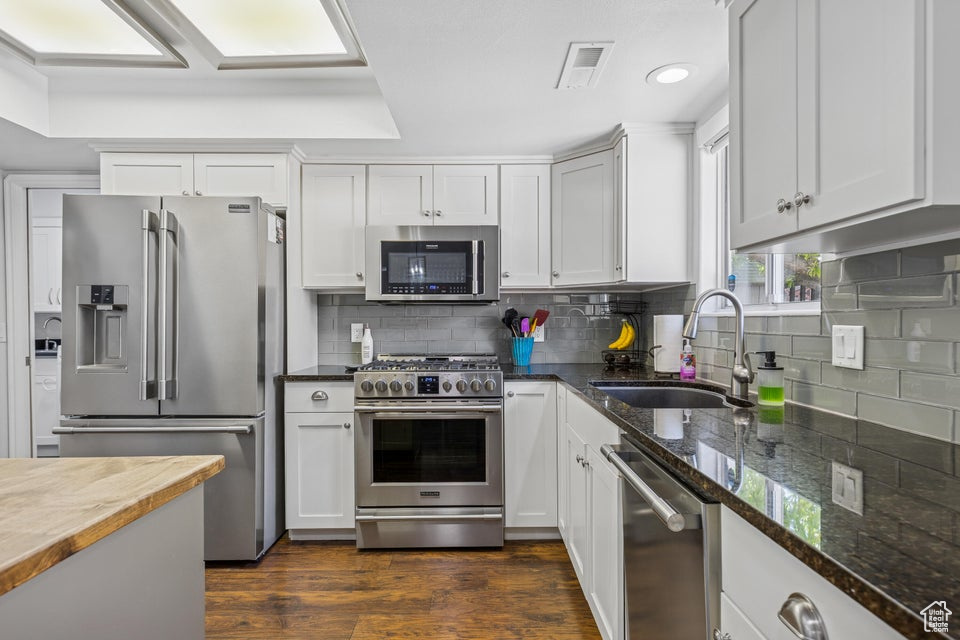 Kitchen with stainless steel appliances, dark stone counters, backsplash, dark wood finished floors, and recessed lighting