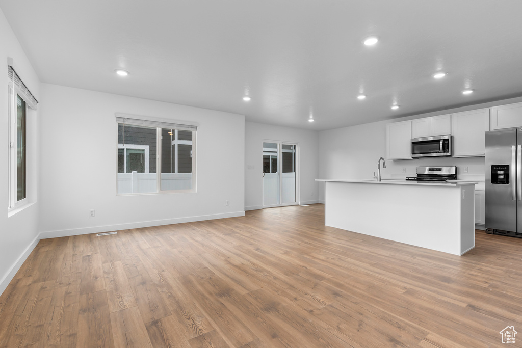 Kitchen featuring appliances with stainless steel finishes, recessed lighting, light wood-type flooring, light countertops, and a kitchen island with sink