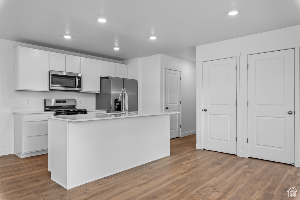 Kitchen with stainless steel appliances, light wood-style floors, a kitchen island with sink, white cabinets, and recessed lighting