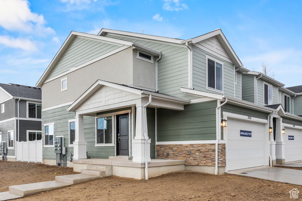 Multi unit property featuring a garage, driveway, covered porch, and stone siding