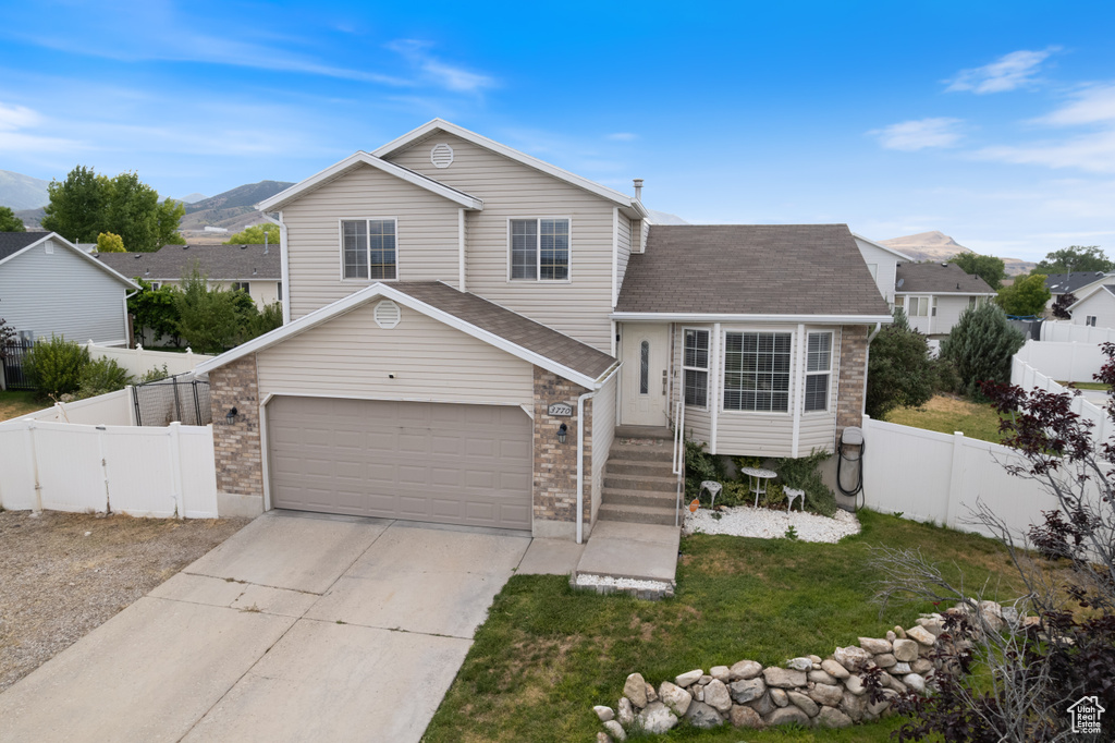 Tri-level home with driveway, a mountain view, roof with shingles, and brick siding