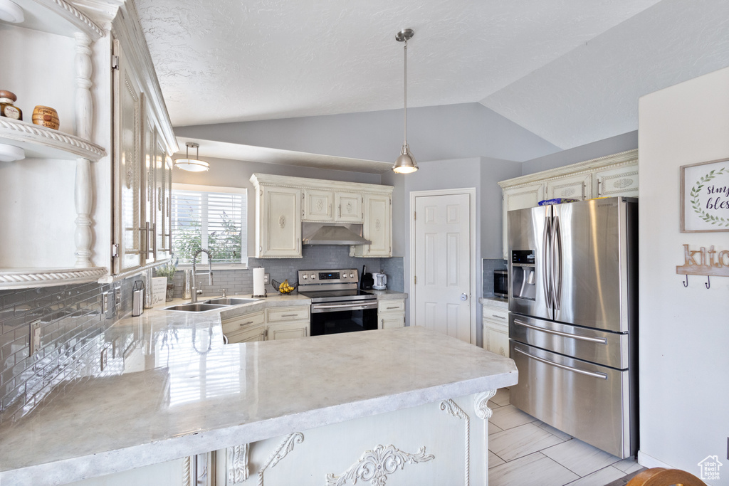 Kitchen featuring appliances with stainless steel finishes, under cabinet range hood, a peninsula, vaulted ceiling, and decorative backsplash