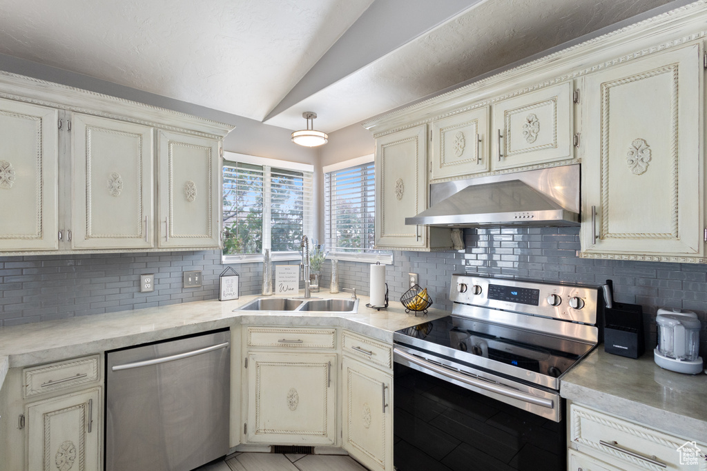 Kitchen with stainless steel appliances, under cabinet range hood, tasteful backsplash, light countertops, and vaulted ceiling