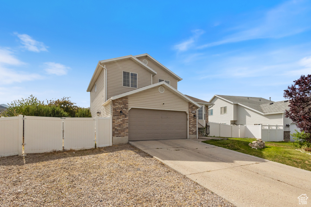 Traditional home featuring driveway, an attached garage, brick siding, and a gate
