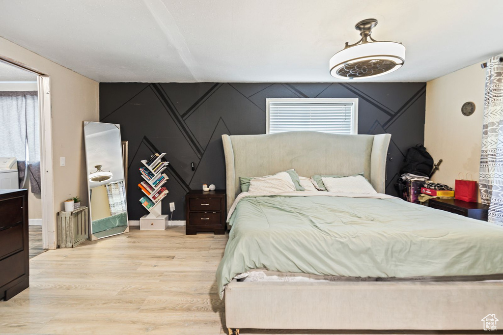 Bedroom with light wood-style flooring, washer / clothes dryer, and an accent wall