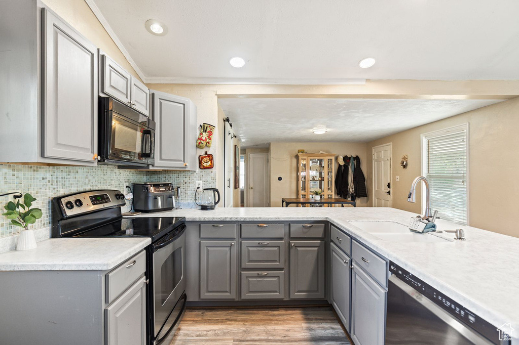 Kitchen with gray cabinetry, appliances with stainless steel finishes, light wood-type flooring, light countertops, and tasteful backsplash