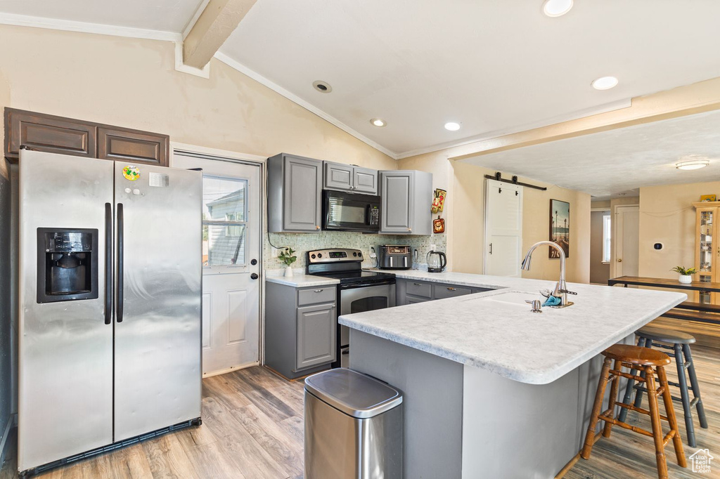 Kitchen with appliances with stainless steel finishes, gray cabinetry, light wood-style flooring, light countertops, and a peninsula