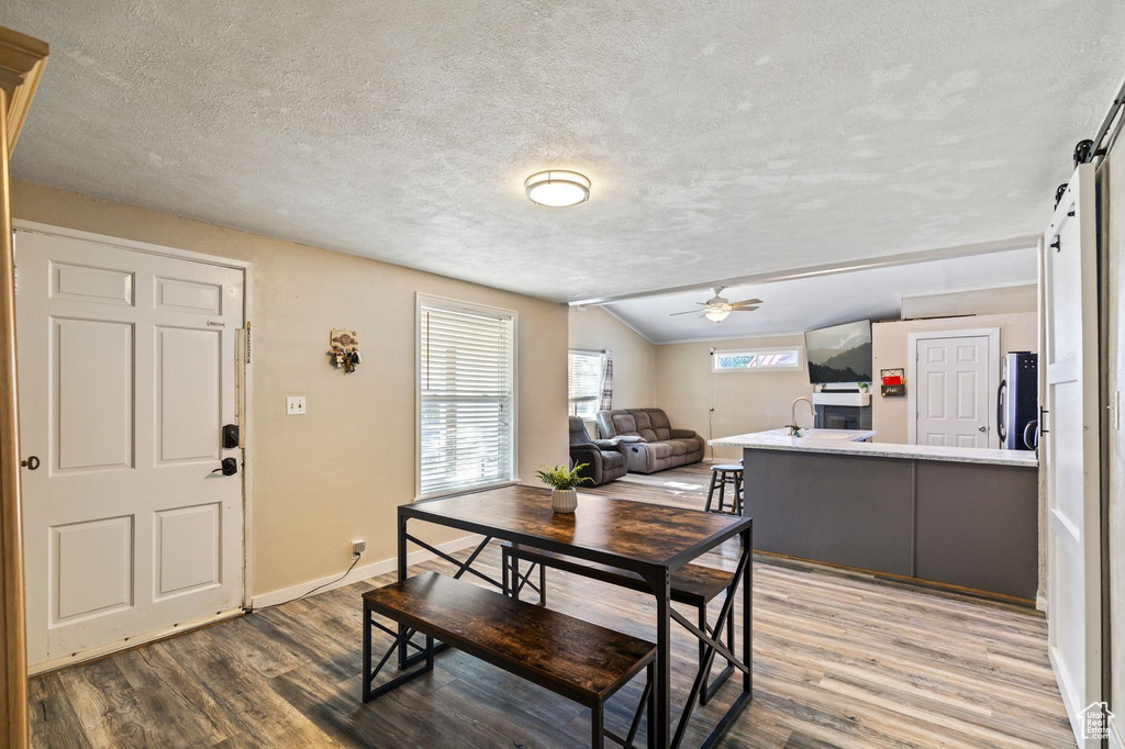 Dining area with vaulted ceiling, wood finished floors, a textured ceiling, ceiling fan, and a barn door