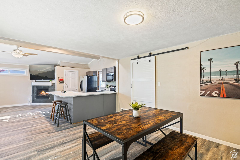 Dining room with light wood-type flooring, a barn door, ceiling fan, a warm lit fireplace, and vaulted ceiling