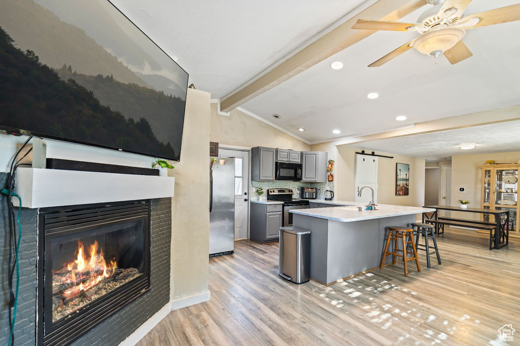 Kitchen featuring gray cabinetry, appliances with stainless steel finishes, light wood-type flooring, a glass covered fireplace, and light countertops