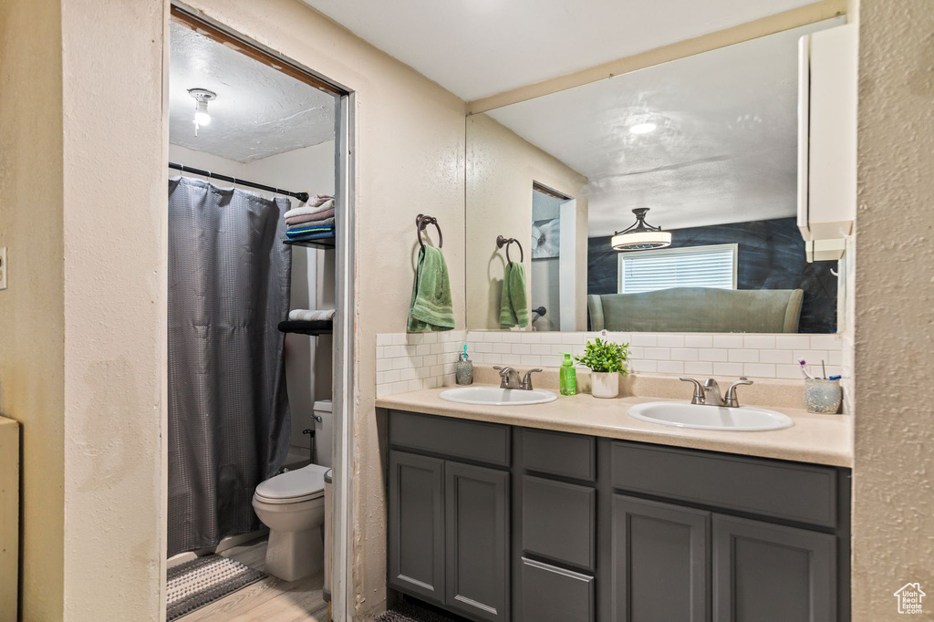 Full bath featuring decorative backsplash, double vanity, wood finished floors, curtained shower, and a textured wall