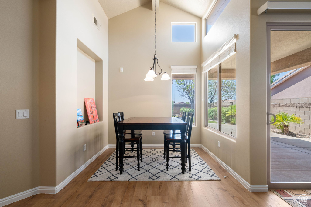 Dining space with a chandelier, wood finished floors, healthy amount of natural light, and high vaulted ceiling