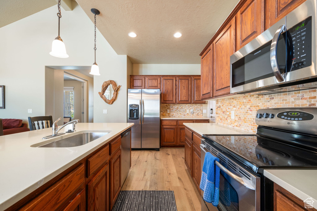 Kitchen with appliances with stainless steel finishes, light countertops, light wood-style flooring, brown cabinets, and lofted ceiling