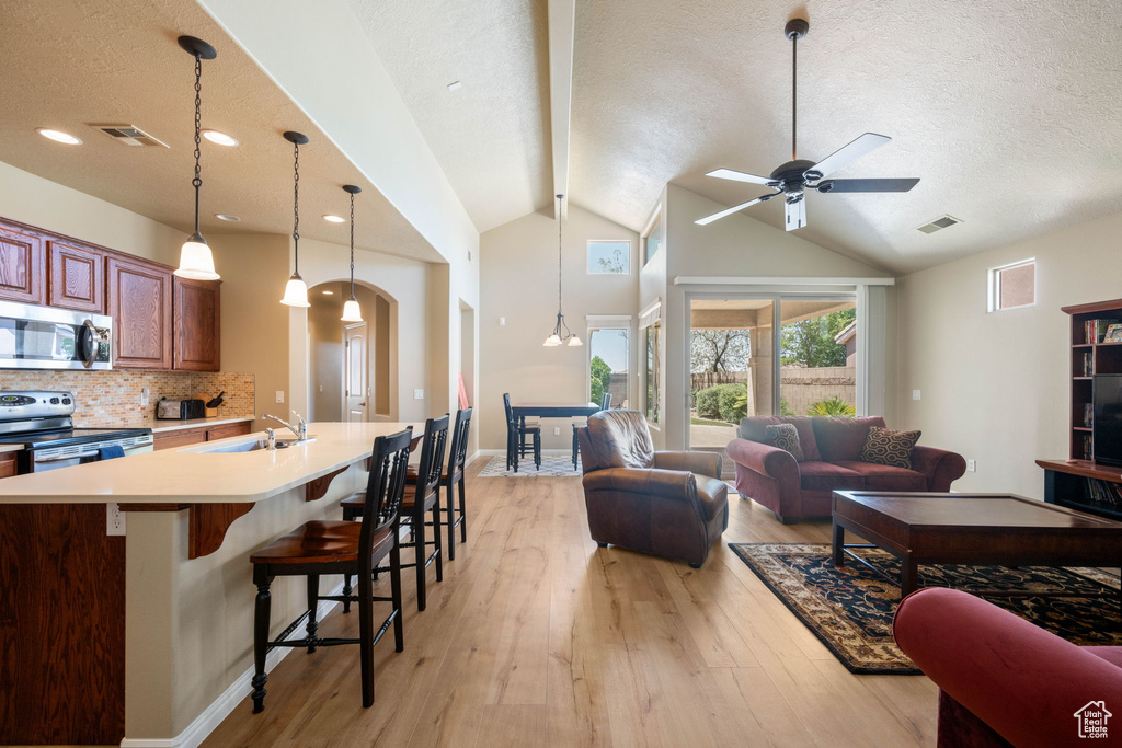 Kitchen with stainless steel appliances, open floor plan, a textured ceiling, a breakfast bar area, and light wood-type flooring