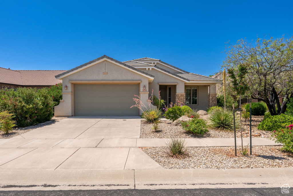 Ranch-style home featuring a garage, stucco siding, driveway, a tiled roof, and stone siding