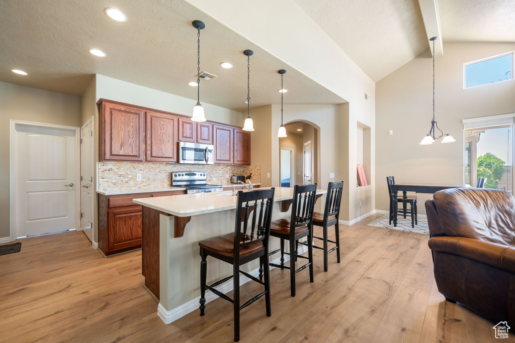 Kitchen featuring appliances with stainless steel finishes, brown cabinetry, light countertops, tasteful backsplash, and light wood-type flooring