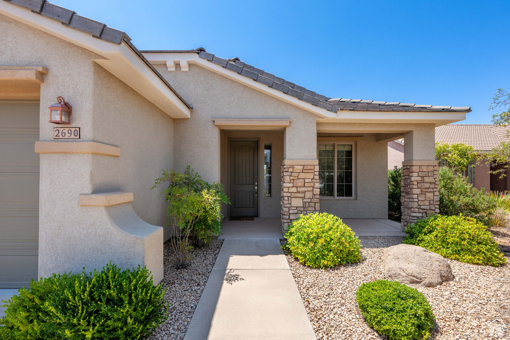 Doorway to property with stucco siding, stone siding, a porch, and a tile roof