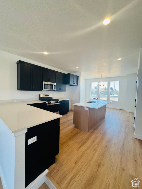 Kitchen featuring appliances with stainless steel finishes, dark cabinets, a chandelier, light countertops, and light wood-type flooring