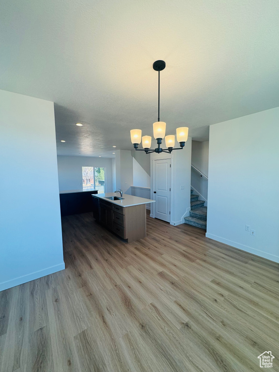 Kitchen featuring open floor plan, light wood-style flooring, a chandelier, a center island with sink, and light countertops