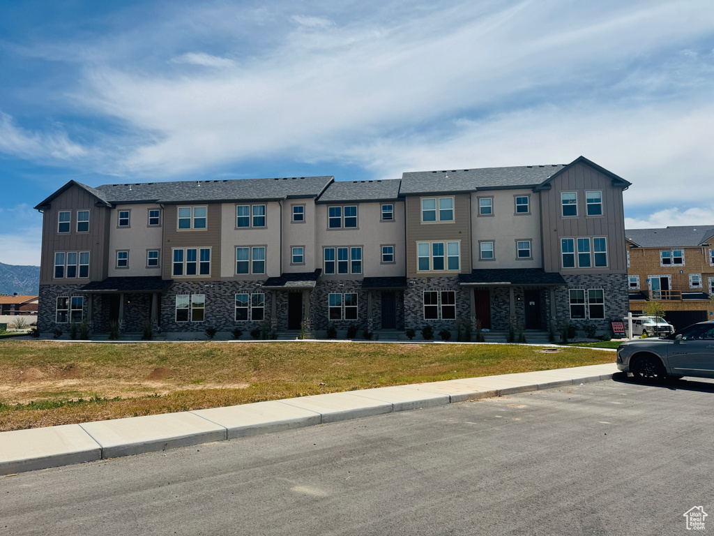 Townhome / multi-family property with board and batten siding, stone siding, a front lawn, and uncovered parking