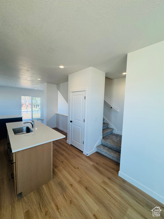 Kitchen with a textured ceiling, light wood-type flooring, a kitchen island with sink, light countertops, and recessed lighting