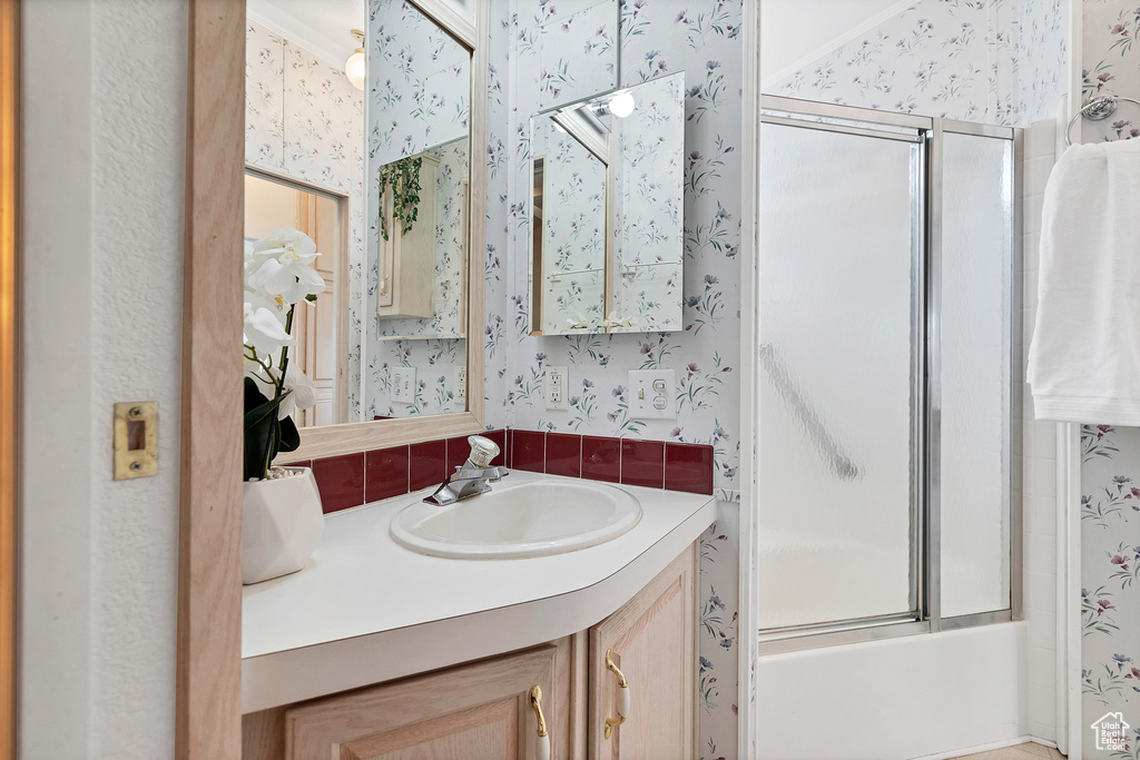 Bathroom featuring wallpapered walls, vanity, and enclosed tub / shower combo