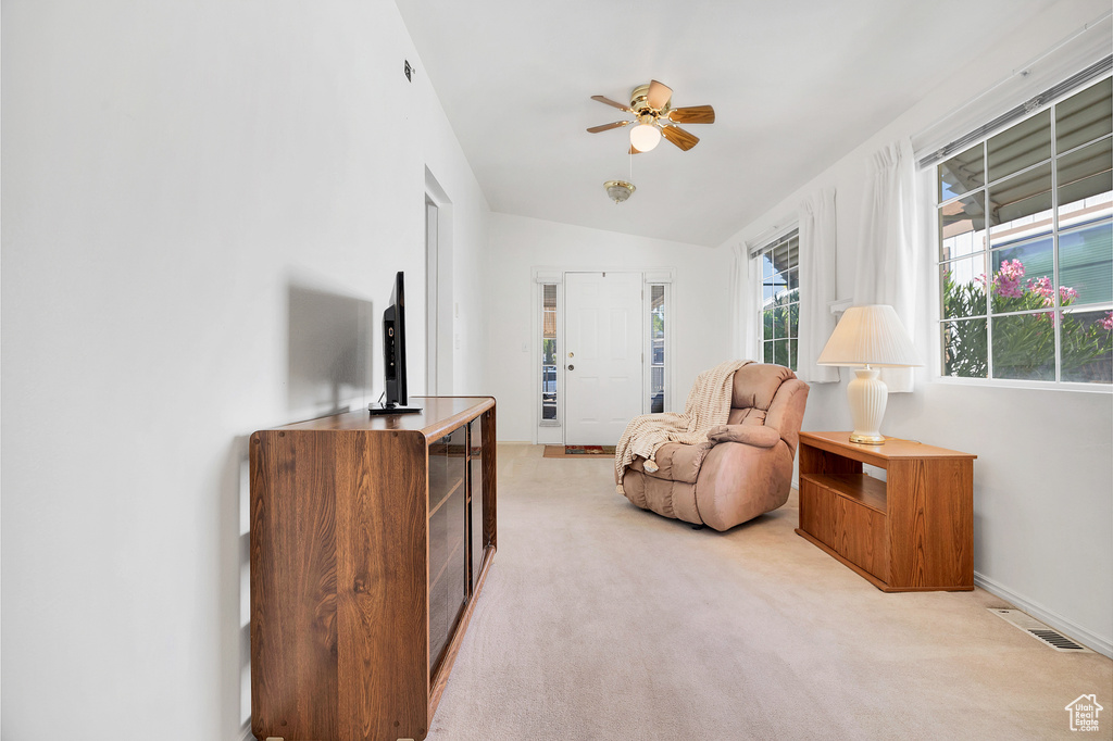 Living area featuring vaulted ceiling, light colored carpet, and a ceiling fan