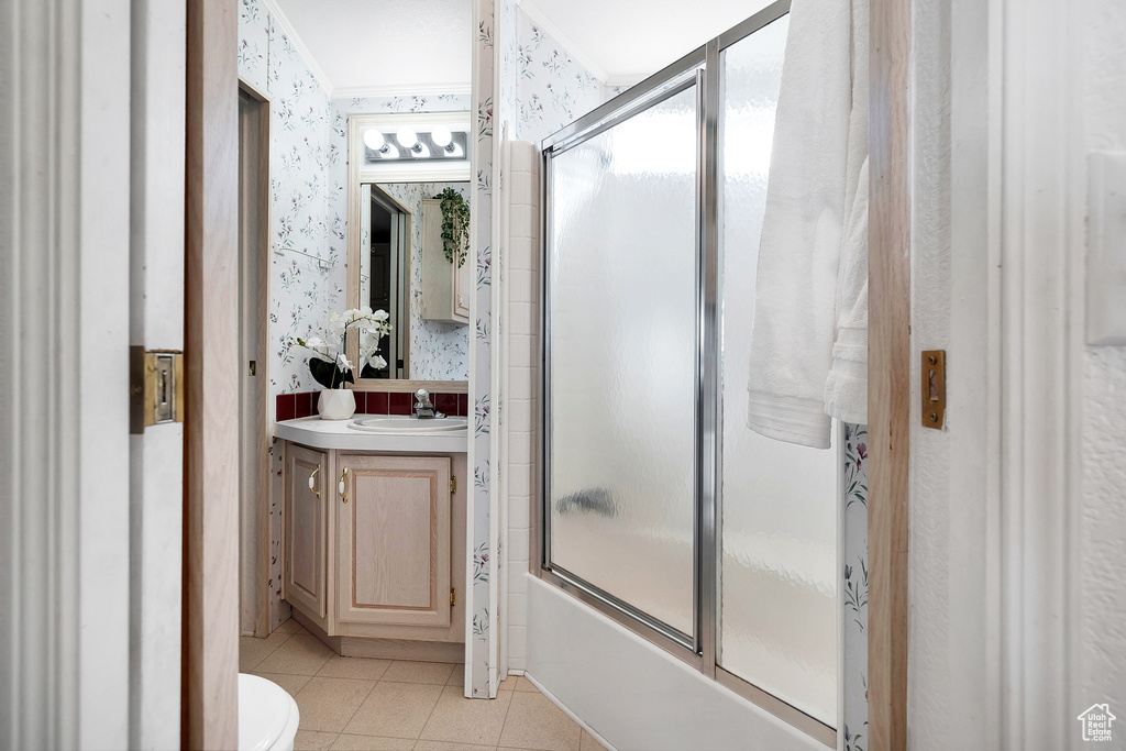 Bathroom with wallpapered walls, vanity, tile patterned flooring, shower / bath combination with glass door, and ornamental molding