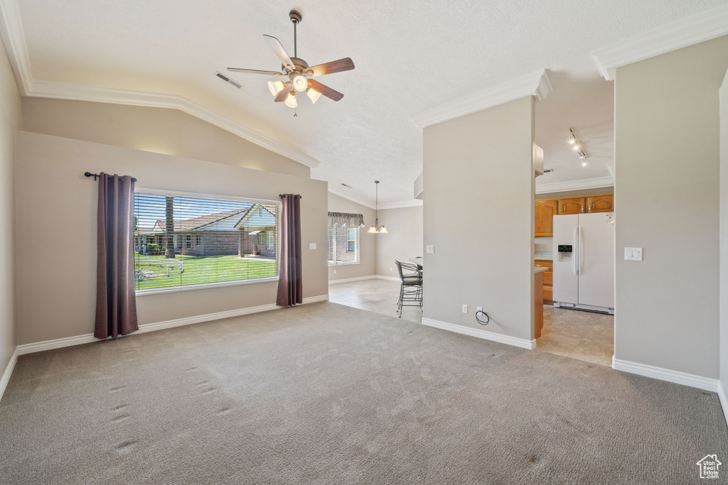 Unfurnished living room featuring ceiling fan, light carpet, vaulted ceiling, and crown molding