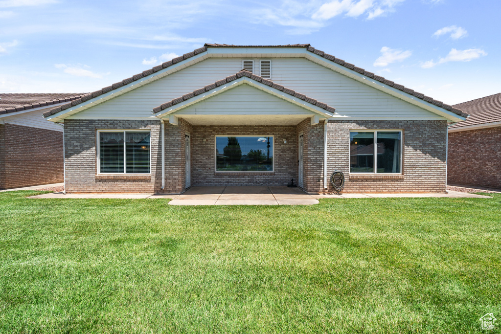 Back of house featuring a patio area, a yard, brick siding, and a tile roof